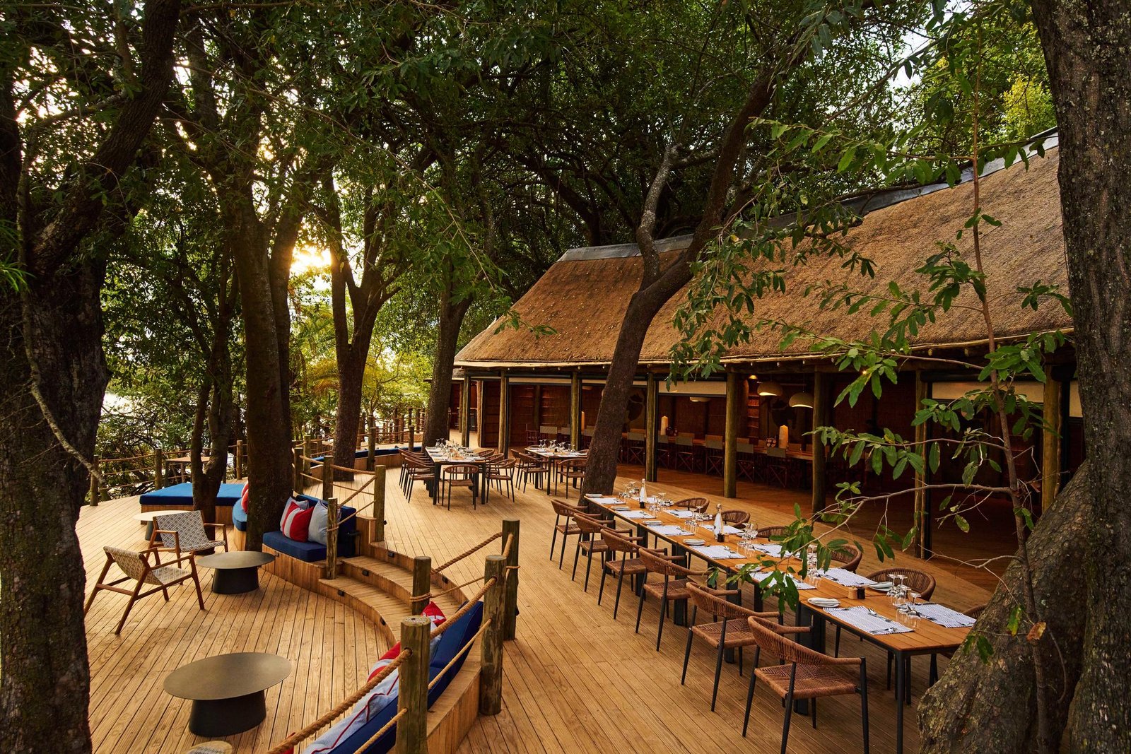 Xugana Island Lodge reetgedecktes Hauptgebäude mit Holzdeck unter Bäumen
