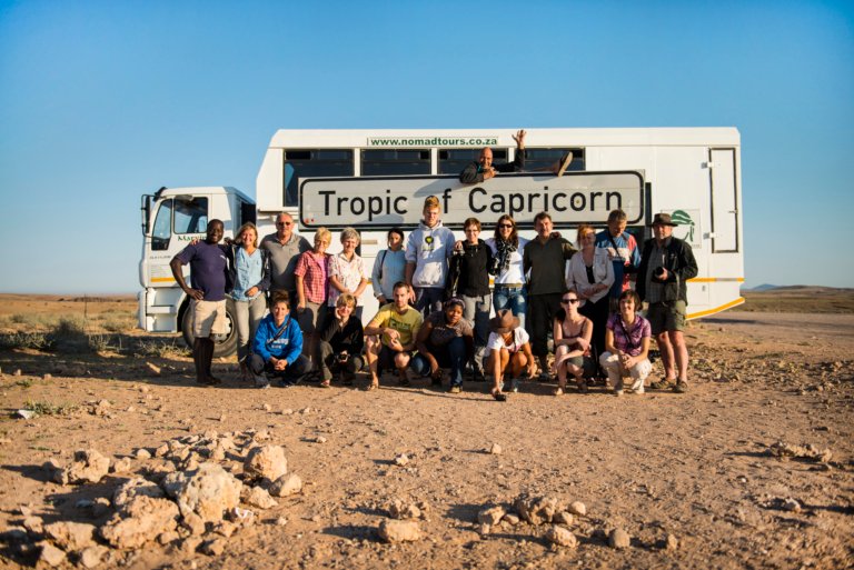 Nomad Africa Tours & Safari Adventure Truck mit Teilnehmer vor dem Tropic of Capricorn Schild in Namibia