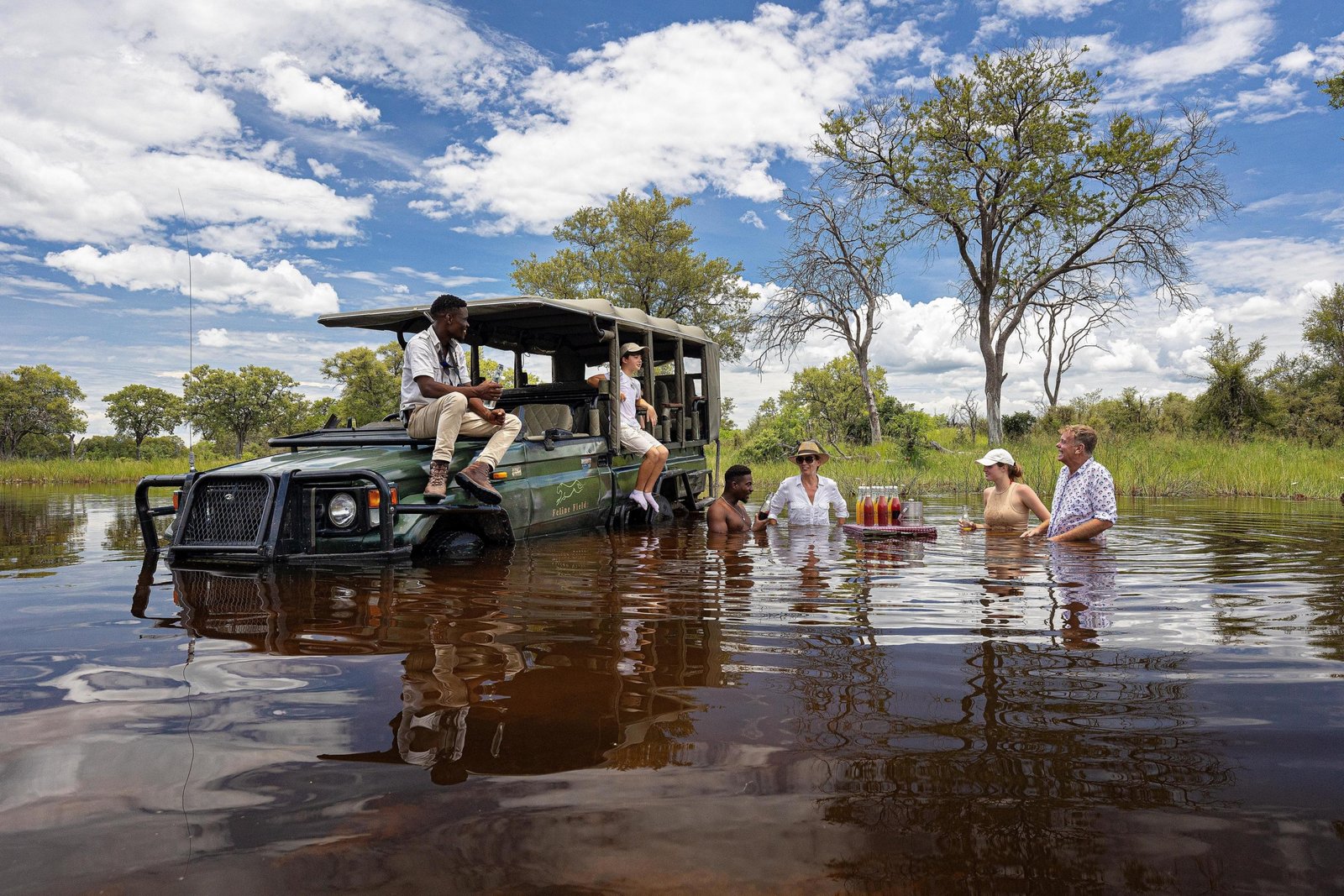 Feline Fields Vintage Camp Sundowner im Wasser mit Getränken und Safarifahrzeug