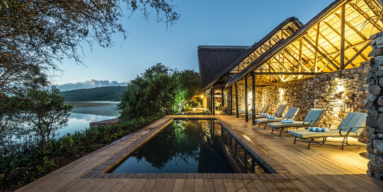 Kariega River Lodge Poolbereich in der Dämmerung mit Liegestühlen und Infinity Pool
