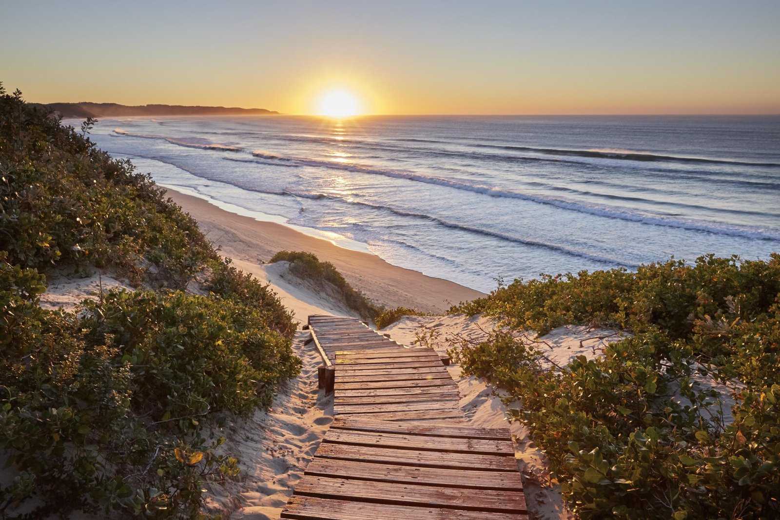 Steg führt zum Meer hinunter mit Sonnenuntergang im Hintergrund