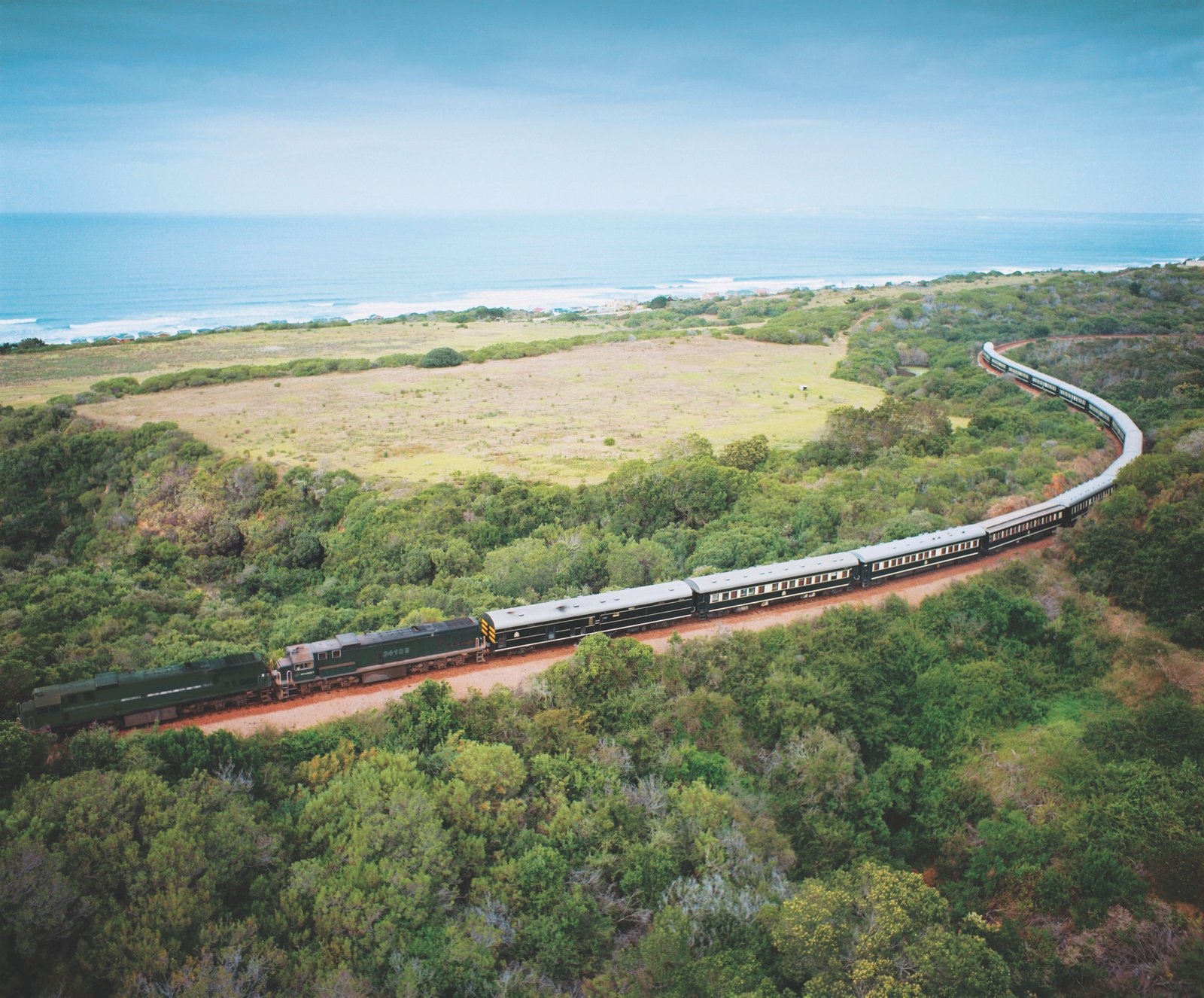 Rovos Rail fährt durch grüne Landschaft mit Meer im Hintergrund