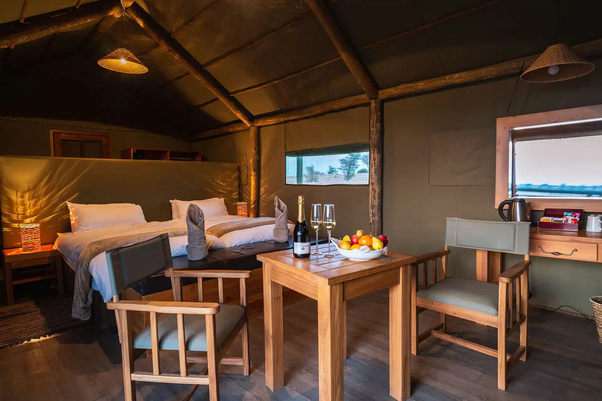 Zeltzimmer mit Bett, Tisch und Stühlen sowie Champagner und Früchteteller.