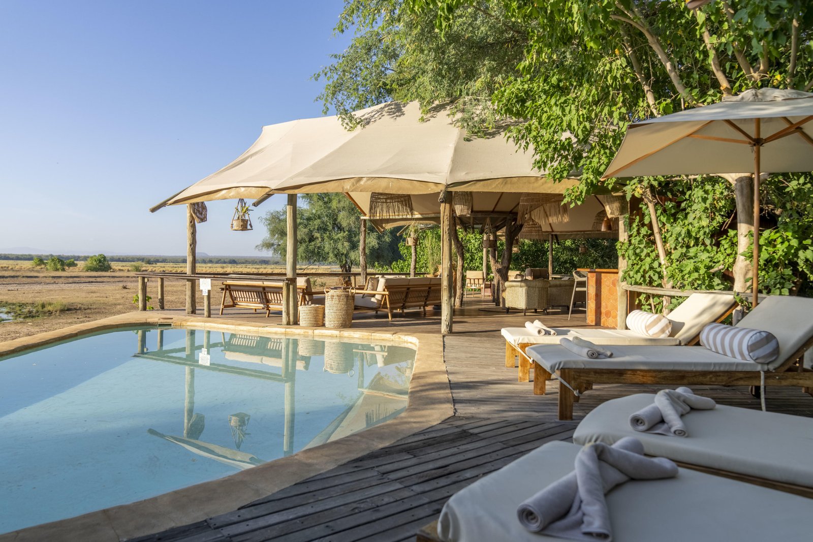Poolbereich mit Sonnenliegen und Blick in die Wildnis