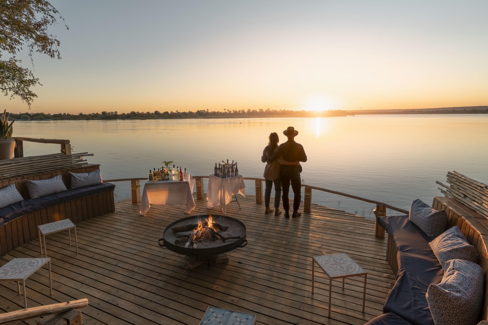 2 Personen auf dem Sunset Deck mit Loungebereich, Feuerstelle und Blick auf den Zambezi bei Sonnenuntergang