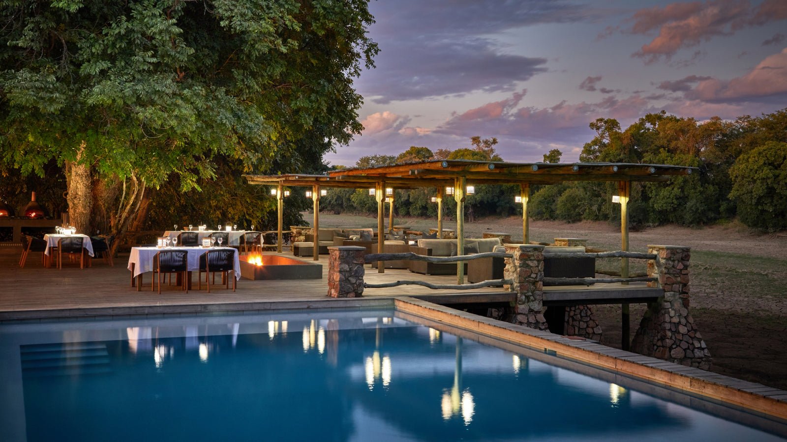 Mfuwe Lodge in Zambia Swimmingpool mit gedeckten Tischen auf der Terrasse bei Abenddämmerung