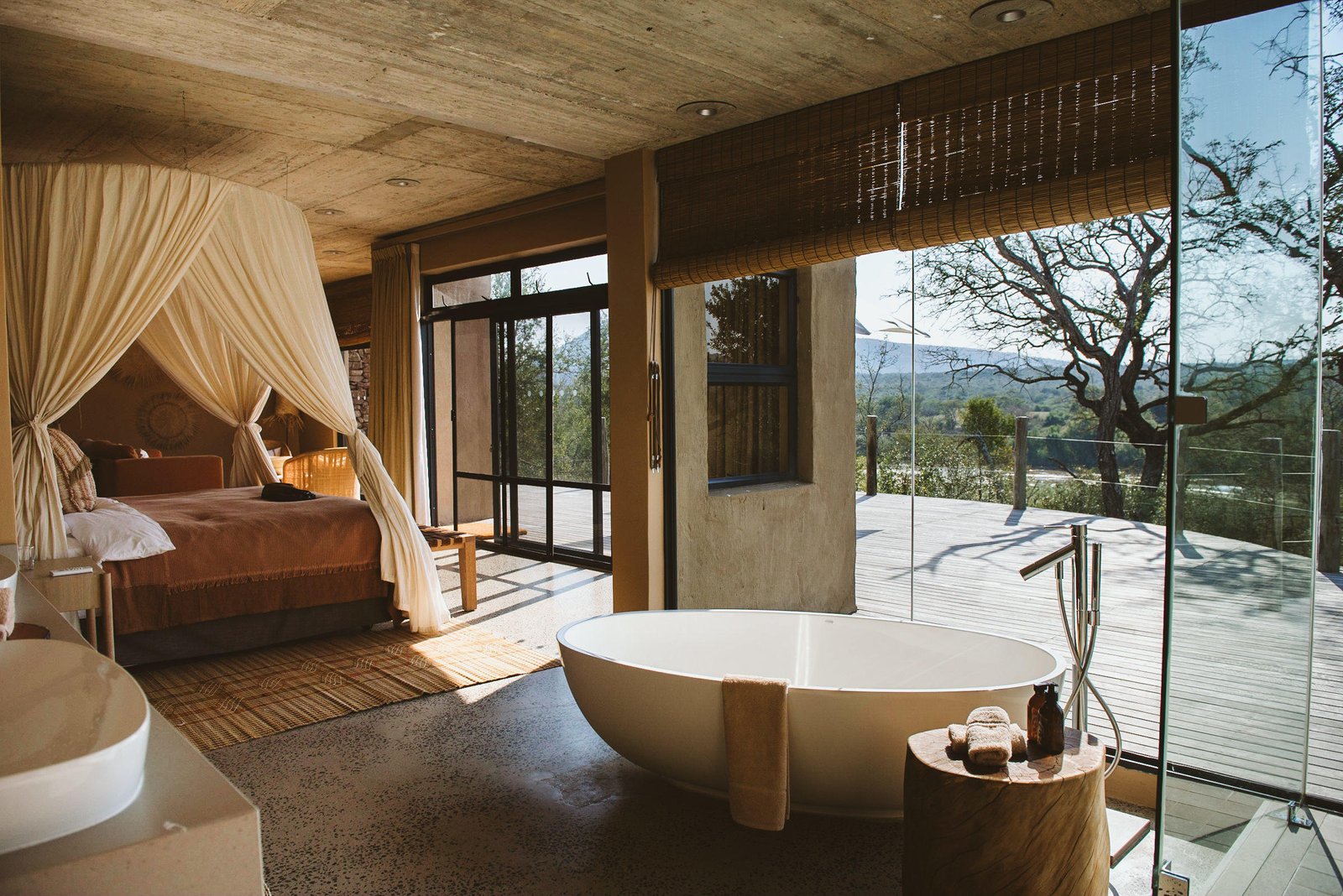 Schlafzimmer mit freistehender Badewanne, gemütlichem Bett und Blick in den Busch